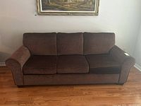 Front view of brown velour sofa showing three loose seat cushions and three back cushions with rolled arm design.