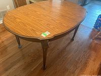 Overall view of the oval wood veneer dining table with decorative legs and one extension leaf inserted, showing wood grain pattern and finish.
