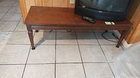 Full view of rectangular wooden coffee table with four legs on tiled floor, remote on top, under TV, showing structure and overall condition.