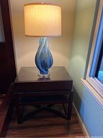 Photo of one dark wood nightstand with blue-green glass lamp turned on.