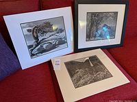 Three Ansel Adams photographic prints placed on a red couch, one framed and two unframed with white mattes.