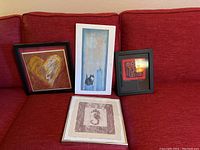 Four framed prints displayed on a red couch showing varied art subjects.