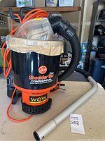 Front and side view of Hoover Pro Shoulder Vac Commercial Backpack vacuum showing clear cover, hose, and orange cord.