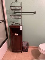 Bathroom cabinet, metal shower caddy, woven storage basket next to toilet and shower stall.