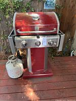 Front view of red Kenmore gas BBQ grill with three control knobs and propane tank on the base.