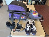 Photo showing the Fireforce bowling ball bag, Winnie the Pooh bowling ball in cover, navy bowling shoes with white laces, black wrist guards, and black socks on a table.