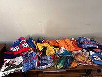 Top view of multiple colorful cycling jerseys neatly folded on a table showing various prints and logos including Run Canada, California Republic, and more.