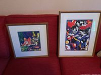 Two framed and matted cat art prints on red couch showing relative size and framing.