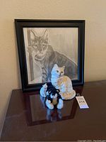 Framed pencil sketch of a tabby cat with three cat figurines on a wooden surface.