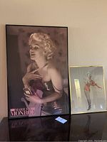 Photo showing two framed Marilyn Monroe art posters, one large and one small, displayed against a wall.