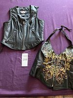 Both black leather Harley-Davidson women's vest and halter top laid flat on purple surface