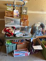 Wide view of the miscellaneous bundle in garage showing storage drawers, wooden organizers, flipped flops, metal bucket, spray bottle, and boxes beneath the table.