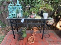 Full view of black metal rectangular table with various outdoor décor items including lanterns, ceramic planters, metal stands, plants, and small sculptures.