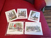 Set of 5 unframed 8 x 10 Paris art prints displayed on a red couch, showing each print laid out and clearly visible.