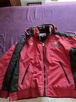 Front view of red and black San Francisco 49ers jacket laid flat on purple surface, showing full front zipper and pockets.