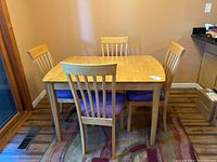 Photo of small rectangular light wood dining table with 4 matching chairs with blue padded seats.