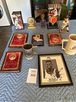 Overview of sports memorabilia including plaques, figurines, trophies, drinkware, and signed photo on cloth surface