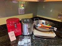 Overview of lot showing red airtight container, toaster, cookie sheets, wok pan, and kitchen utensils on granite counter