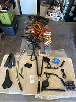 Overview of all bike parts laid out on floor and mat, showing seats, handlebars, tires, and small accessories.