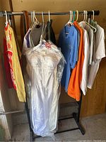 Full view of clothes rack holding multiple shirts and wedding dress wrapped in plastic