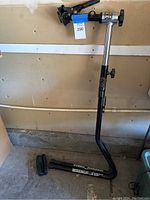 Full photo of the black and silver bike repair stand with base, clamp, and adjustable height post in a garage setting.