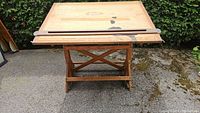 Front view of oak drafting table top flat, showing wear spots and X-frame base