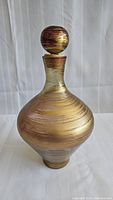Full view of the purple tinted art glass decanter with gold stripes and spherical stopper.