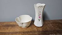 Photo of two Belleek pottery pieces: shamrock bowl and trellis lily vase on wooden surface against gray background