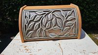 Front view of wooden bread box showing curved door with raised leaf pattern panel