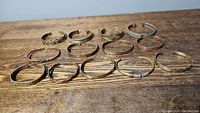 Overview of 18 copper and brass handmade cuff bracelets arranged on a wooden surface showing variety in style and color.