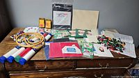 Overview of entire cross stitch crafting lot showing hoops, floss, ribbon, patterns, and fabric pieces spread on table.
