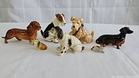View of all 7 ceramic dog figurines arranged on a white surface, showing various breeds and detail