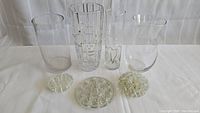 Four glass vases and three glass flower frogs arranged on white cloth background