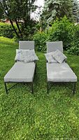 Pair of gray outdoor lounge chairs with matching patterned throw pillows on green grass background.