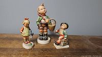 Three Hummel figurines displayed together on table.