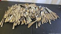 Photo showing a large assortment of silver plated forks, knives, and spoons piled together on a black surface.