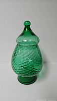 Full view of the green blown glass apothecary jar with lid on, showing diamond optic texture and bulbous shape.