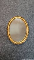 Full view of the oval mirror showing the gold decorative frame and reflective glass surface.