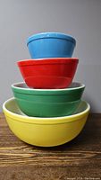 Stacked view of four Pyrex mixing bowls in yellow, green, red, and blue showing exterior colors and shape.