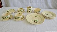 Full set displayed on table, showing all components including plates, cups, saucers, creamer, sugar bowl, and serving plate with consistent Lynn pattern swirl design in green, brown, and black on cream base.