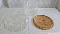 Three clear glass items: embossed Flora salad bowl with botanical details, tulip emboss pattern serving plate, and clear glass bowl on cork base