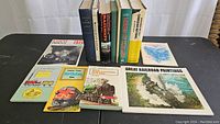 Overview of ten train and railroad books of varying size including hardcover and softcover, arranged standing in back and laid open in front on black surface.