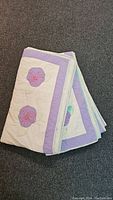 One folded quilt showing edge and two pansy appliques with embroidery on cream background and lavender border.