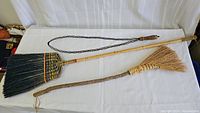 Photo showing entire lot: vintage rug beater and two handmade brooms laid flat on a white surface.