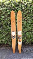 Full view of the pair of vintage wooden water skis standing upright outdoors, showing bindings and wood texture.