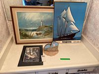 Tabletop display of four nautical-themed art items including framed oil painting, maritime print, stamp print, and painted mushroom.