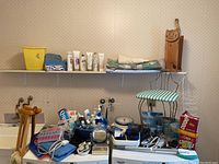 Photo showing bathroom scales, vanity bench with blue and white striped cushion, assorted hair and skin products on shelf, a yellow container, folded linens, handcrafted wooden toilet paper holder shaped and carved with a cat face at top, wire shower caddy and more on laundry machines.