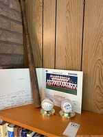 Photo showing 1991 Toronto Blue Jays autographed team photo, two autographed baseballs in plastic cases with gold-tone bases, and a vintage wooden baseball bat on a wooden shelf.