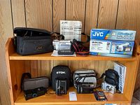 Photo showing the whole lot with JVC video camera, cases, manuals, and other cameras on wooden shelf