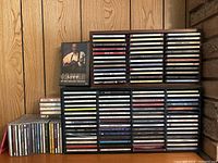 Photo showing several racks filled with CDs and box sets arranged against a wooden wall paneling background.
